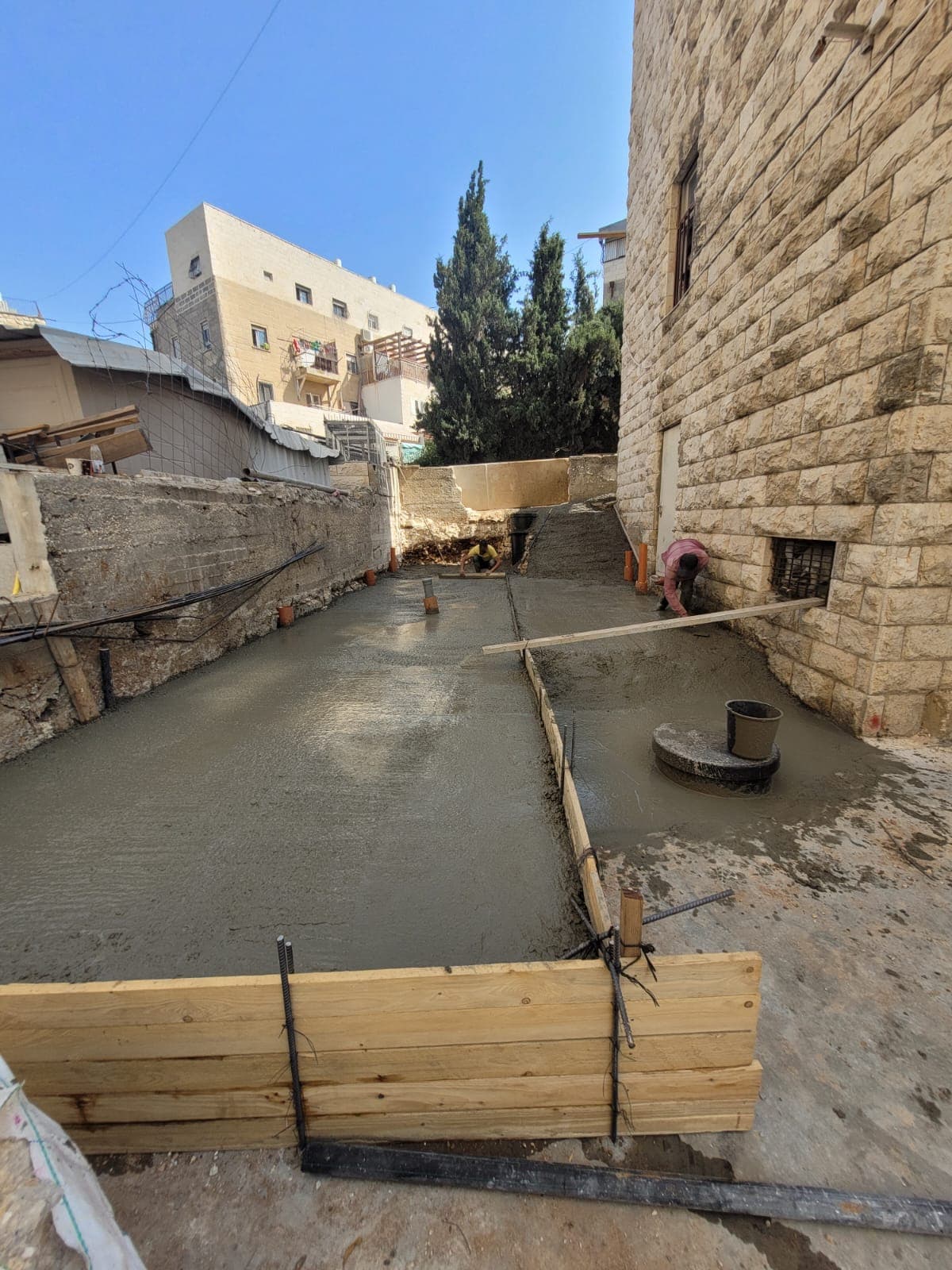 יציקת בטון רחבה בין בניינים, פועלים מחליקים את המשטח