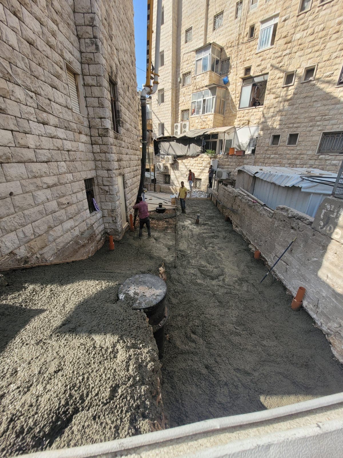 המשך יציקת הבטון על משטח בין שני בניינים