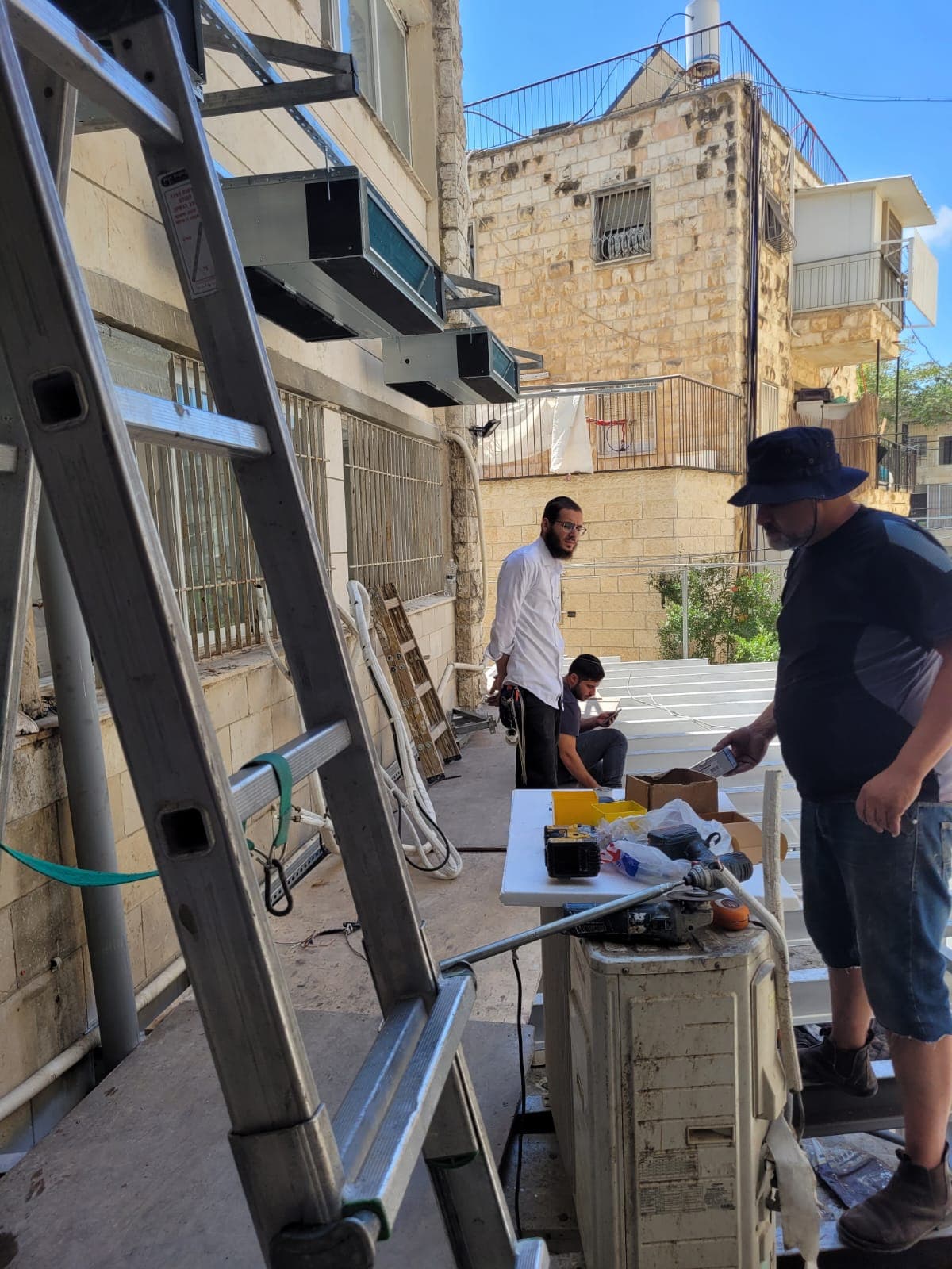 פועלים מכינים לוחות לבנים על שולחן עבודה לצד מבנה אבן
